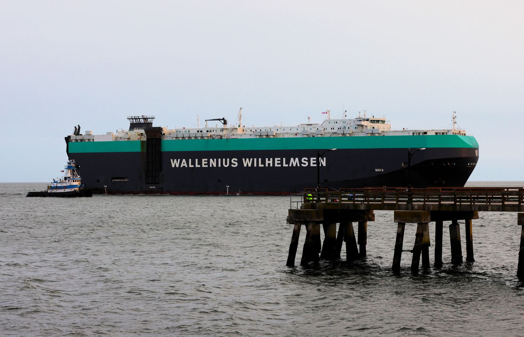 Ro-ro vehicle carrier leaving a harbour with a tug alongside