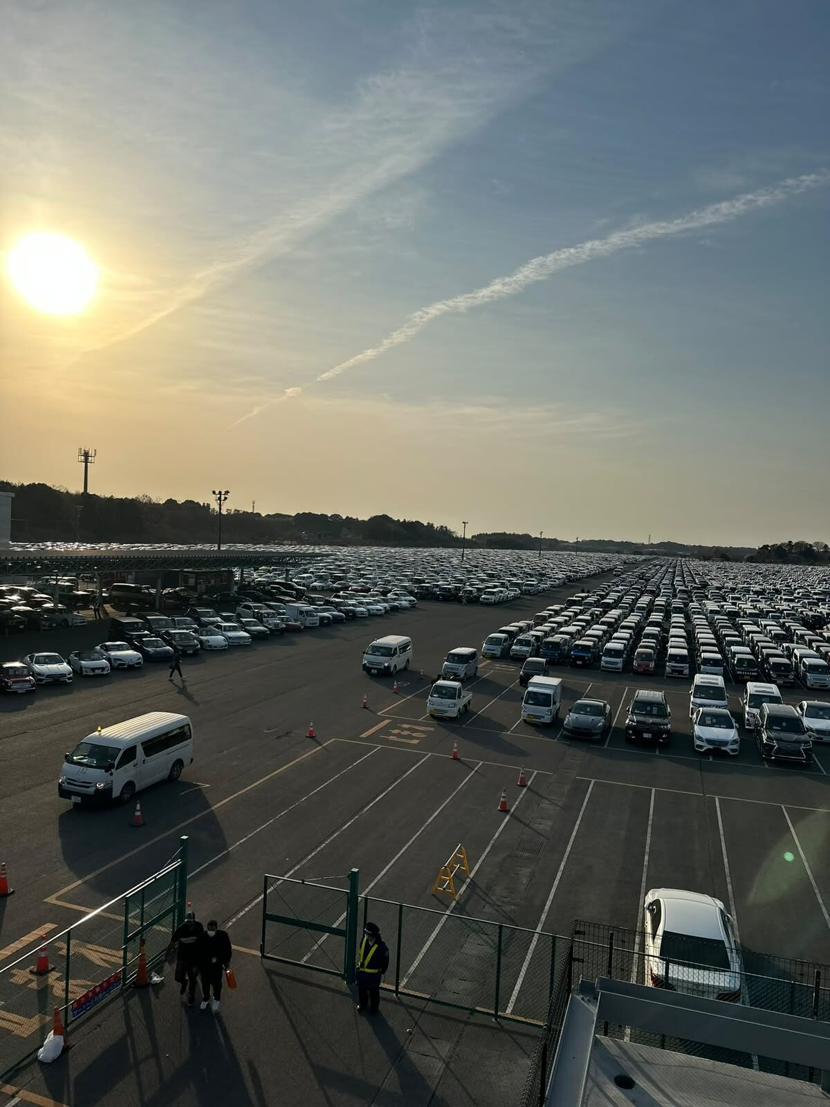 Sunset over rows of vehicles in a Japanese vehicle yard, with staff working in the foreground
